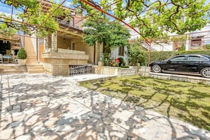 Ein von Grün umgebener Innenhof mit Pflasterung, auf der rechten Seite ist ein Auto geparkt. Ein Gebäude mit Balkon schließt den Hof ein.