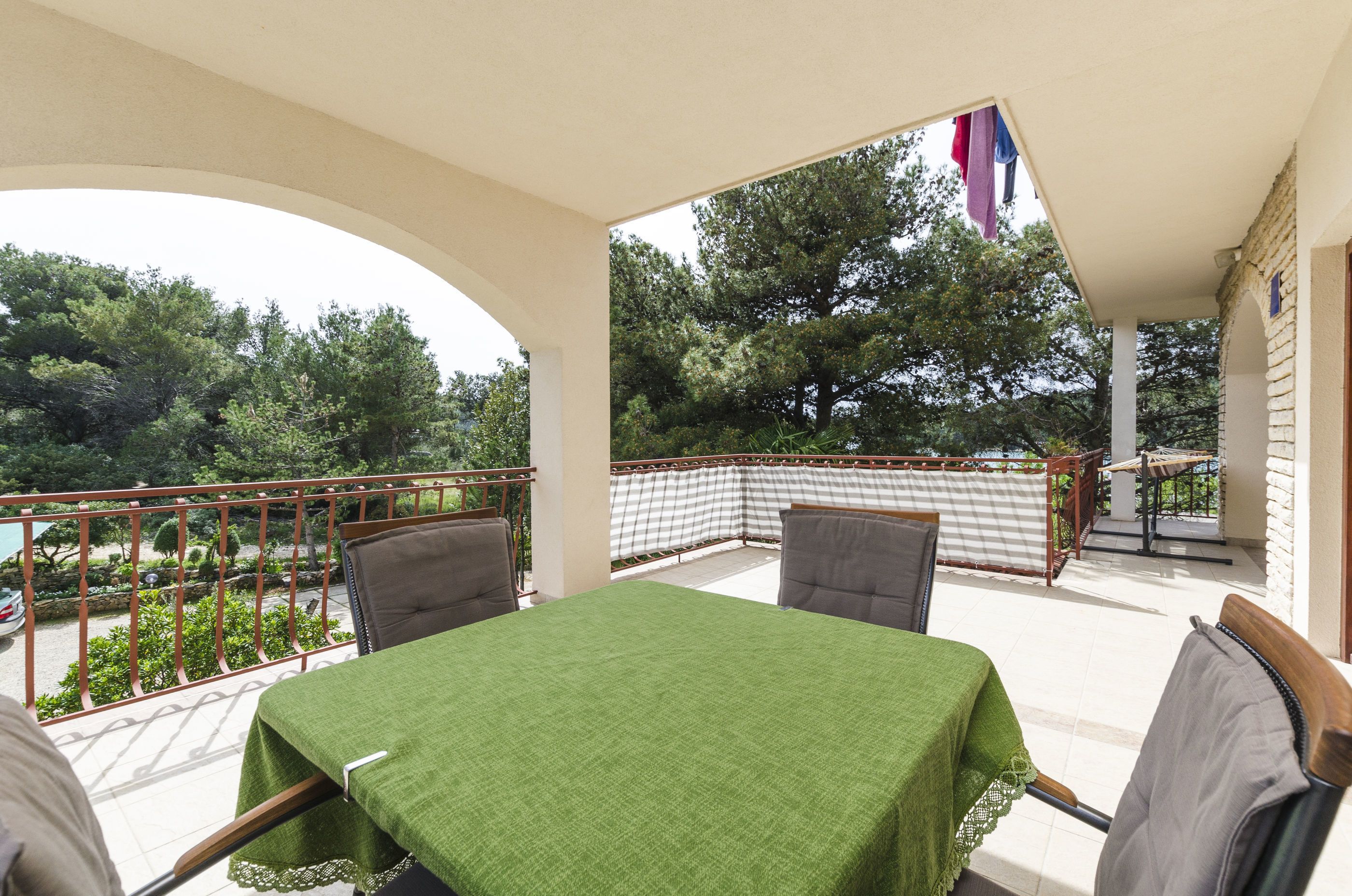 A balcony with a table and chairs, a checkered bench, and a view of trees and a parked car.