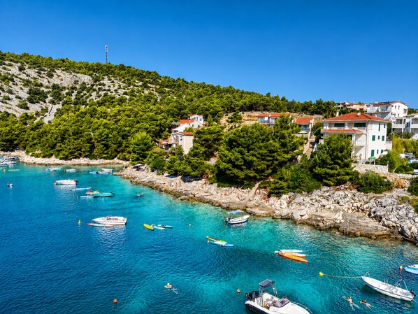 A coastal village with boats docked along the shore, buildings with red roofs, and a clear blue sky. - Apartment Veronika (Razanj)