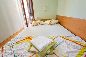 A neatly made bed with a colorful quilt, a wooden headboard, and a window with blinds. - Apartment Veronika (Razanj)