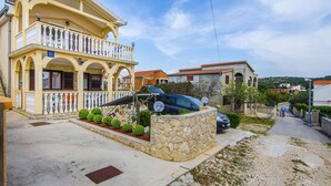 Un edificio a due piani con un balcone, un muro in pietra e un'auto parcheggiata davanti.