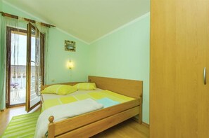Une chambre avec un lit en bois, un tapis à rayures vertes, une porte-fenêtre coulissante donnant sur un balcon et un luminaire fixé au mur.