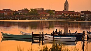 A calm waterfront with several boats docked, a prominent church tower, and residential buildings along the shore. - Apartment Sime (Nin)