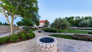 A stone pathway leading to a circular stone well, surrounded by neatly trimmed bushes and trees. - Apartment Sime (Nin)