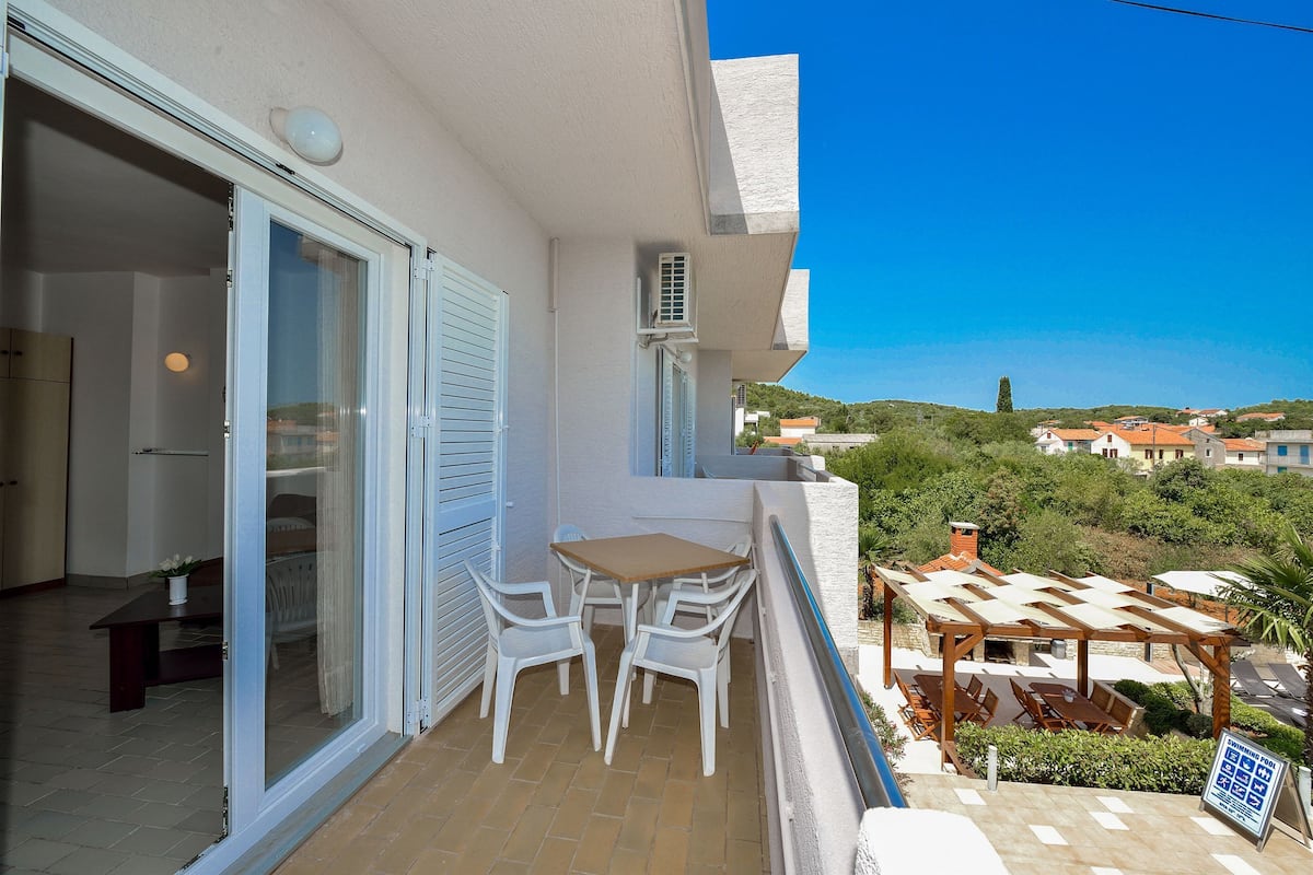 A balcony with a table and chairs, a pergola, and a view of the surrounding area.