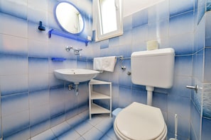 A bathroom with a sink, mirror, toilet, and blue-tiled walls.