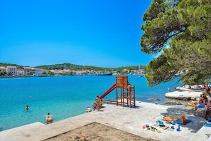 A waterfront playground with a slide, beach chairs, and a sandy area.