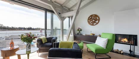 Un salon moderne avec une cheminée, une vue sur l’eau et une grande fenêtre.