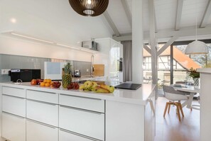 A modern kitchen with white cabinetry, a fruit bowl, and a dining area with a table and chairs.