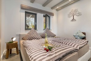 Une chambre avec deux lits, une table de chevet avec une lampe, une bouteille de vin et un verre posé sur le lit.
