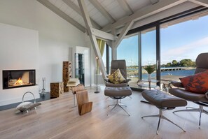 A modern living room with a fireplace, large windows, and a view of the water. - AS1A - Old barn (AS) at c a l l s e n - appartements (Ummanz)