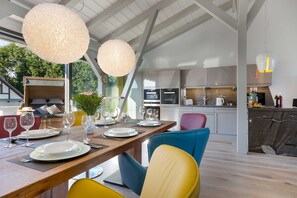 A modern kitchen with white cabinets, a dining area with a wooden table set for four, and a bright, airy space with large windows. - AS1A - Old barn (AS) at c a l l s e n - appartements (Ummanz)