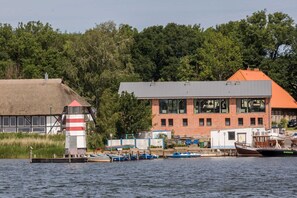 A riverside building with a thatched-roof structure and a modern brick building with large windows. - AS1A - Old barn (AS) at c a l l s e n - appartements (Ummanz)