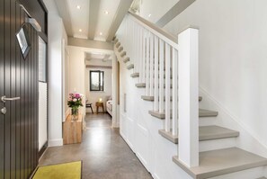 A modern interior with a staircase, a wooden bench, and a vase of flowers.