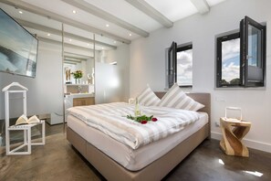 A modern bedroom with a large bed, bedside tables, a mirror, and a view of the sky through open windows.