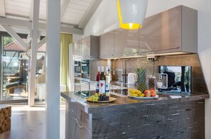 Une cuisine moderne dotée d’un plan de travail en marbre, d’appareils électroménagers en acier inoxydable et offrant une vue sur l’extérieur.