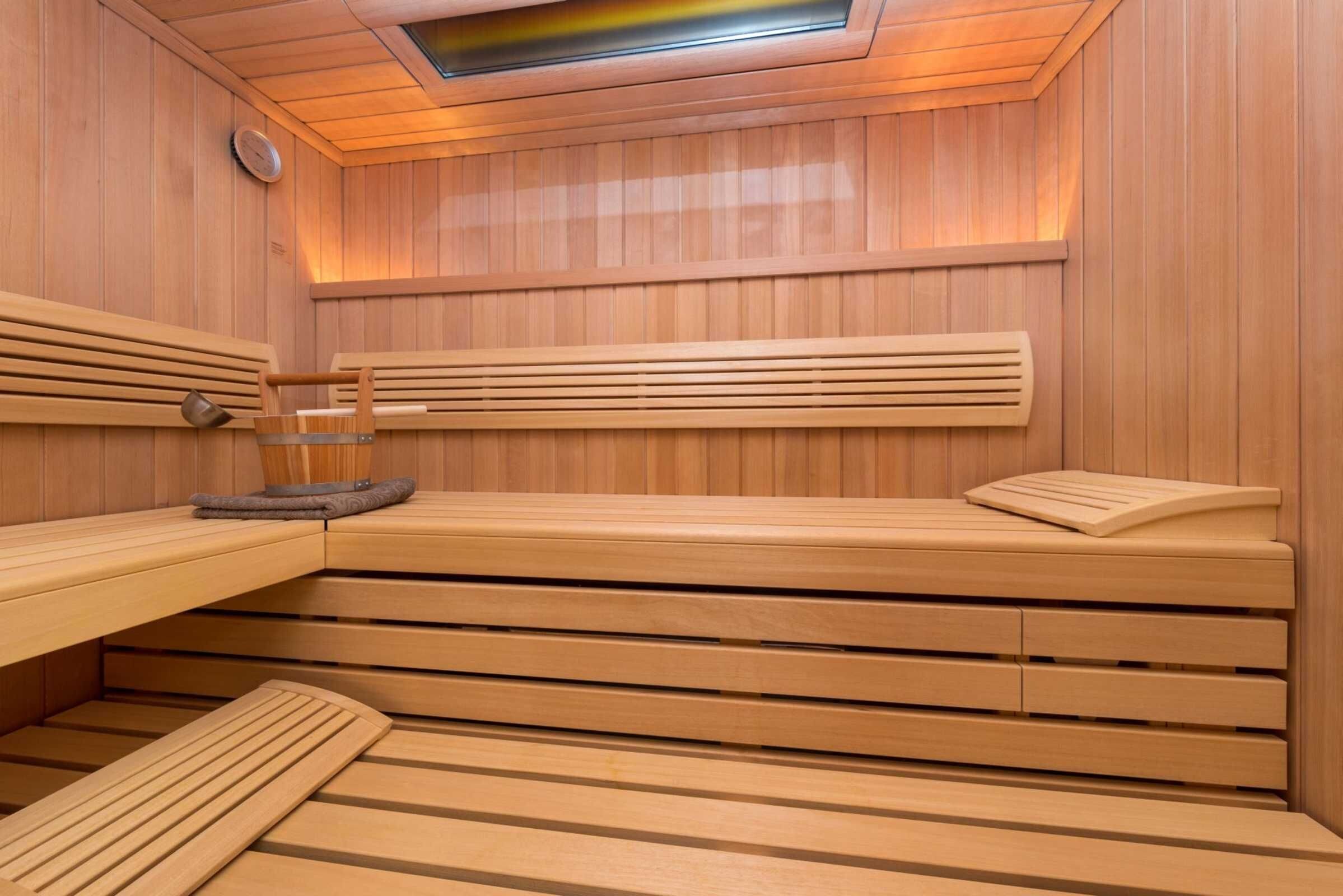 A sauna with wooden benches and benches, a ceiling light, and a wall-mounted control panel.