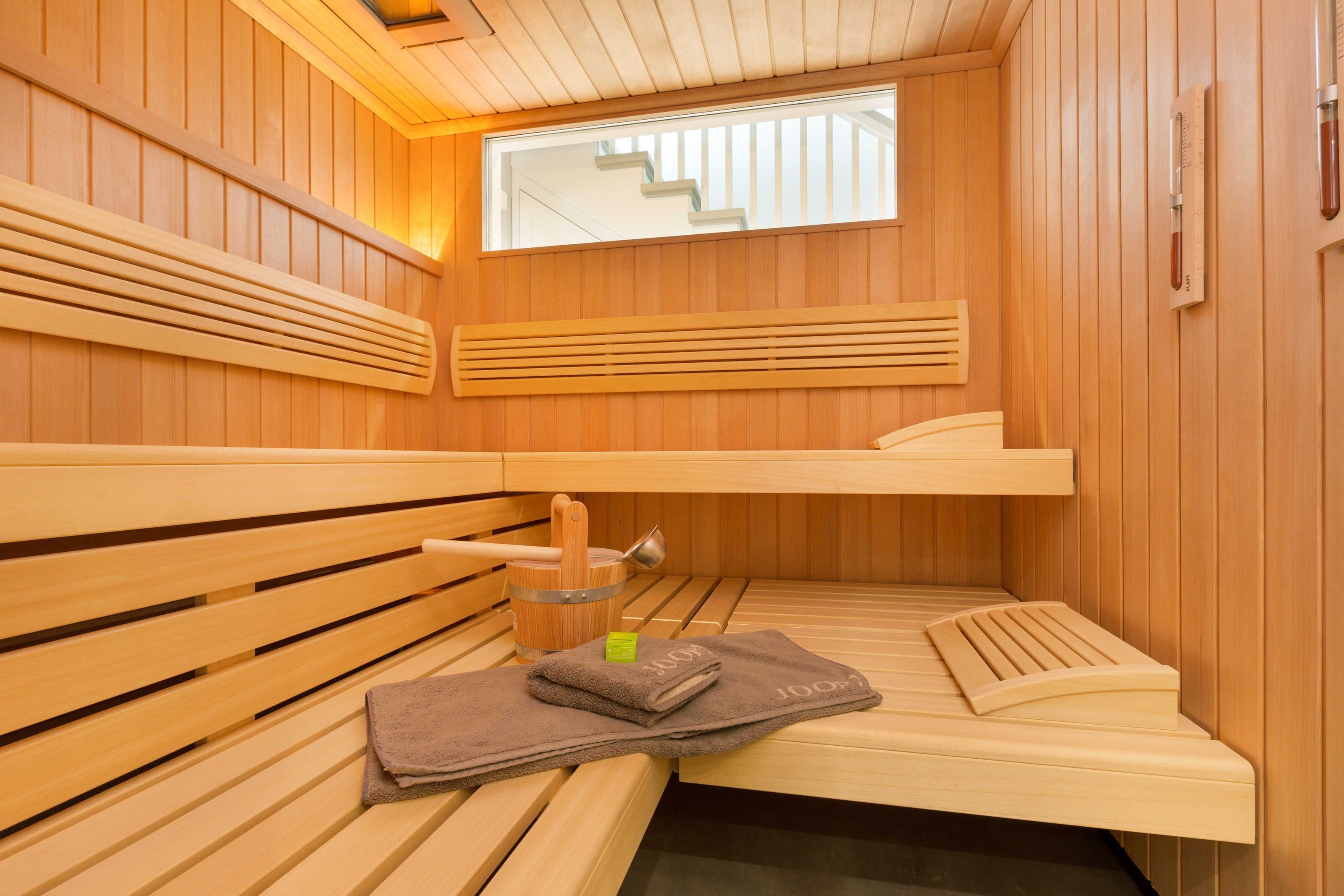 A sauna with wooden benches, a window, and a thermometer on the wall.