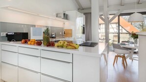 Una cucina moderna con mobili bianchi, una ciotola di frutta e un'area pranzo con tavolo e sedie.