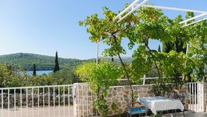 Eine Terrasse mit Tisch und Stühlen, eine Steinmauer und Blick auf einen See und Hügel.