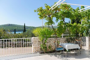 A terrace with a table and chairs, a stone wall, and a view of a lake and hills.