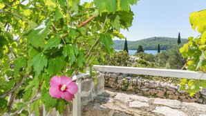 Eine Steinsäule mit einem weißen Geländer, einer rosa Blume und einem Blick auf einen See und Hügel im Hintergrund.