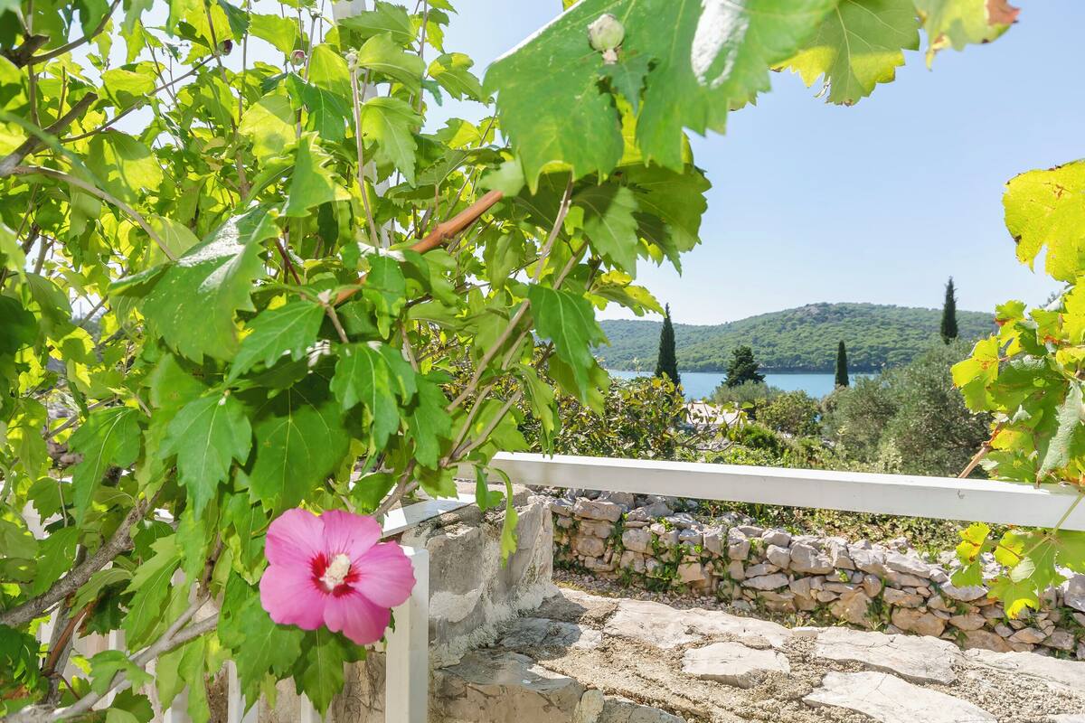 A stone wall with a white railing, a pink flower, and a view of a lake and hills in the background.