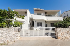 A two-story white building with a stone wall and a white gate.