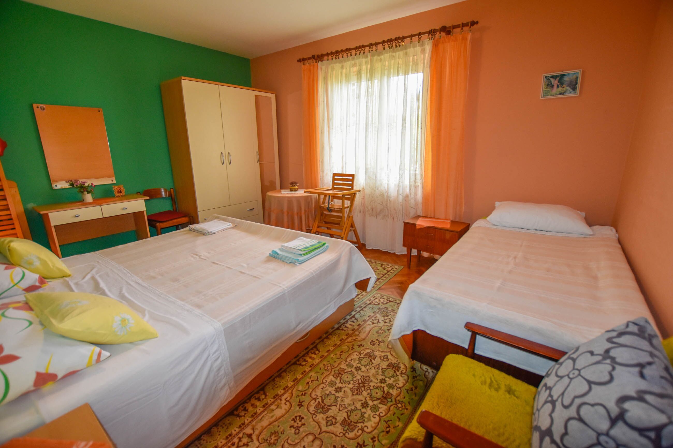 Quarto de hotel com duas camas, uma escrivaninha, um guarda-roupa e uma janela com cortinas.