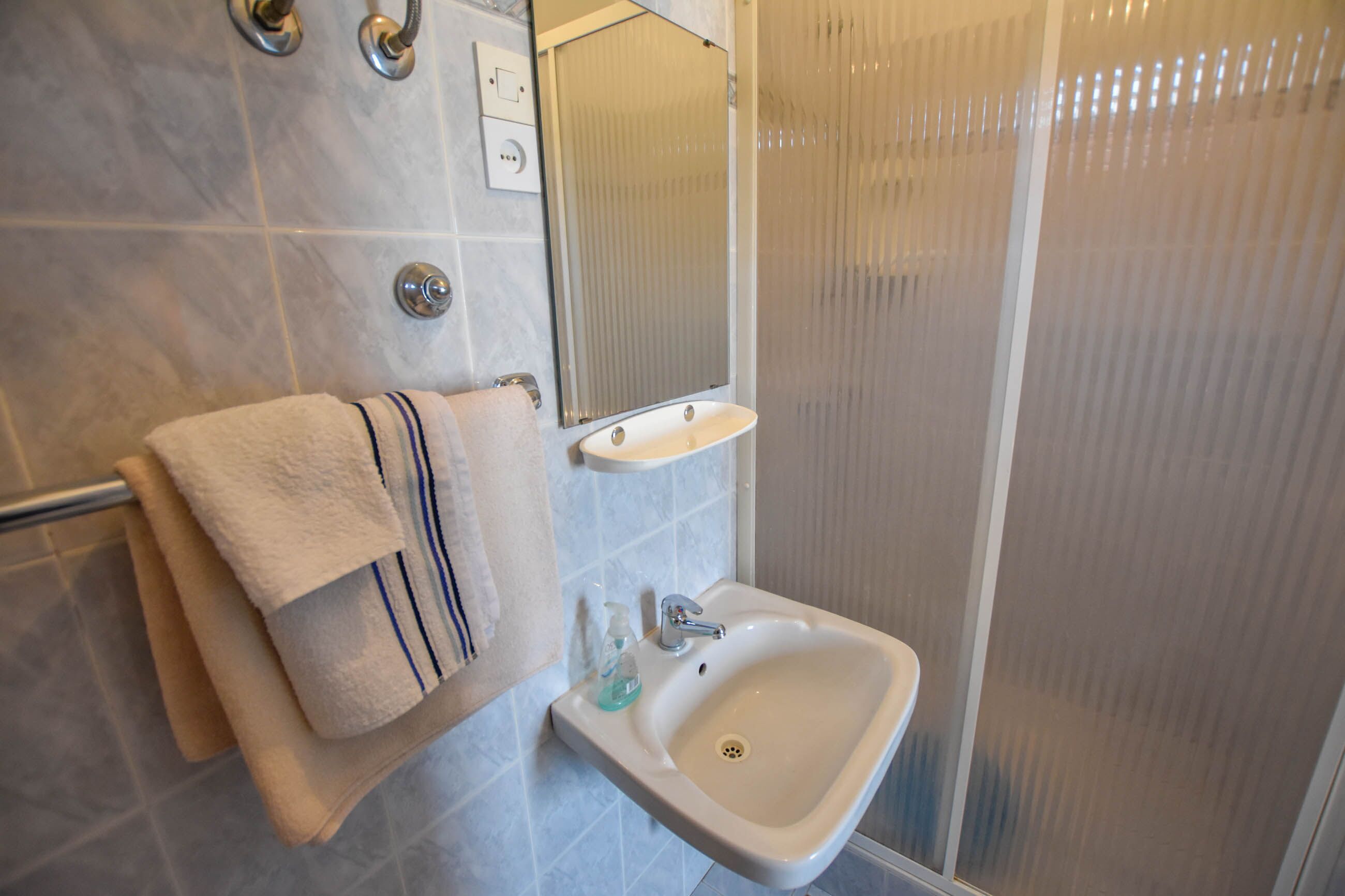 A bathroom with a white sink, a mirror, and a towel rack with towels.