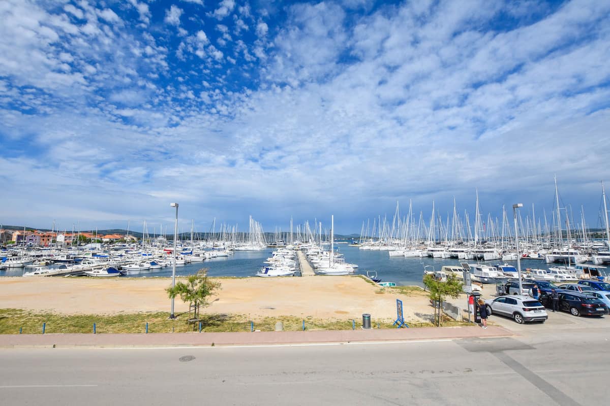 A marina with numerous sailboats docked, a sandy beach, and a clear blue sky.