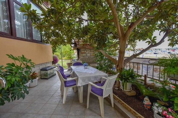 An outdoor patio with a table and chairs, surrounded by potted plants and a view of boats.