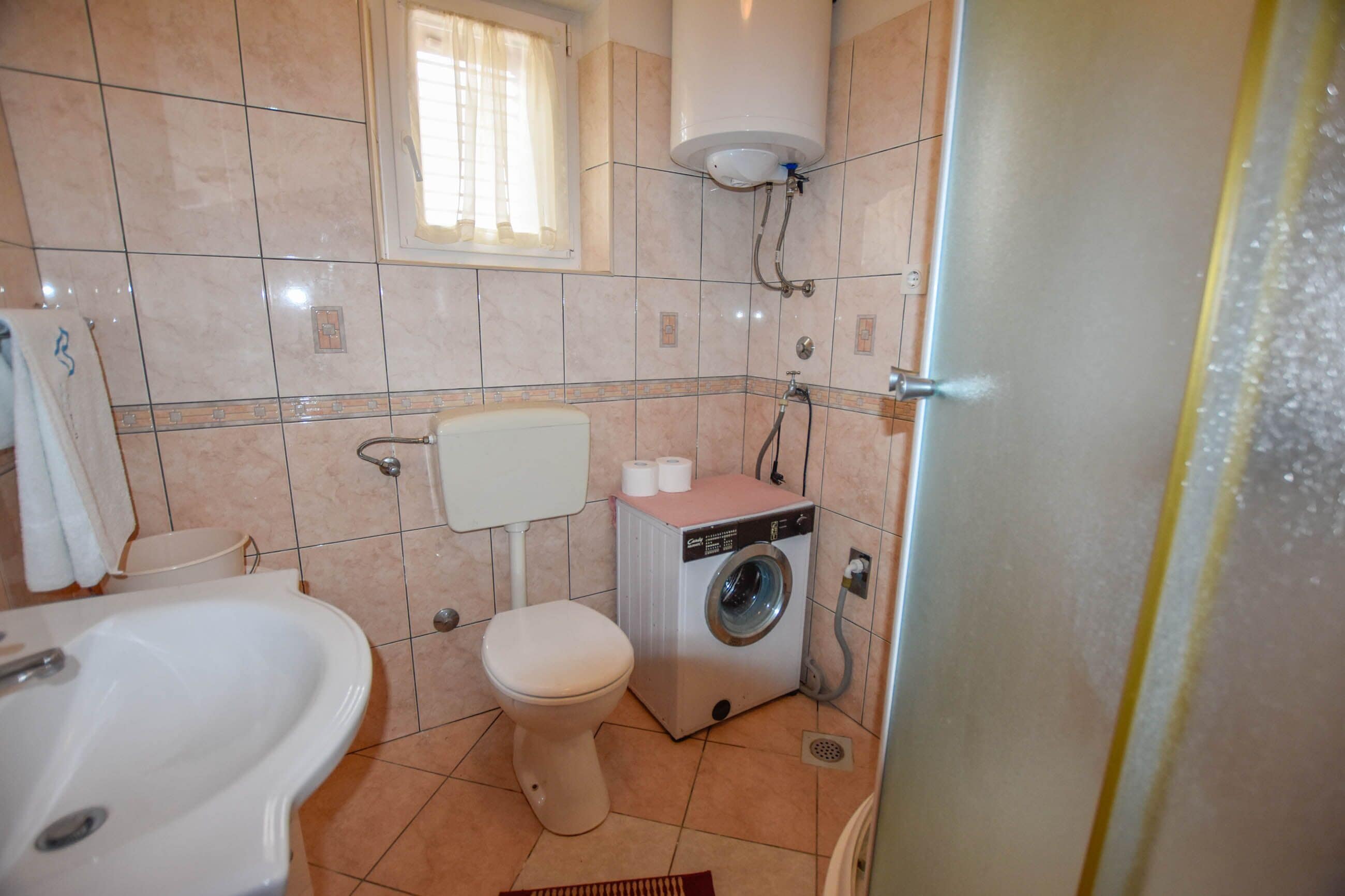 Een badkamer met een bad, toilet, wasmachine en een raam met gordijnen.