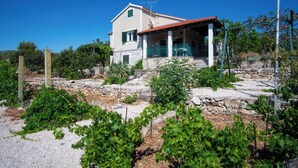 Ένα διώροφο σπίτι με θεμέλια από πέτρα, κόκκινη κεραμοσκεπή και ένα πράσινο μπαλκόνι.