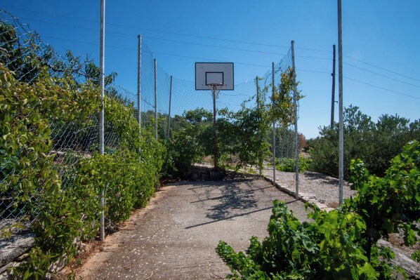 An outdoor basketball court with a chain-link fence, surrounded by greenery. - House Marija (Primosten)