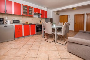 A compact kitchen with red cabinets, a dining table with chairs, and a sofa. - Apartments Ema (Rogoznica)