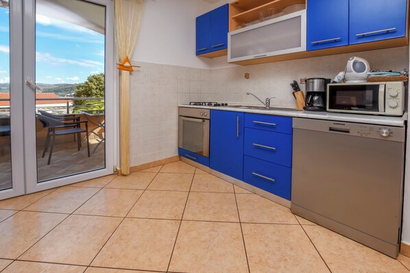 Een keuken met blauwe kastjes, een fornuis, een oven, een magnetron en een vaatwasser.