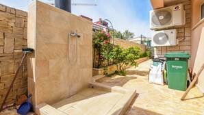A stone-tiled outdoor shower area with a glass enclosure, a stone wall, and a green trash bin. - Apartments Ema (Razanj)