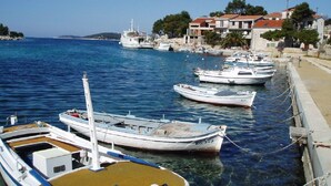 A marina with several boats docked along the waterfront, a clear blue sky, and buildings with red roofs in the background. - Apartments Ema (Razanj)