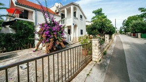 Una calle residencial con una casa blanca que tiene un balcón y un jardín con flores moradas.