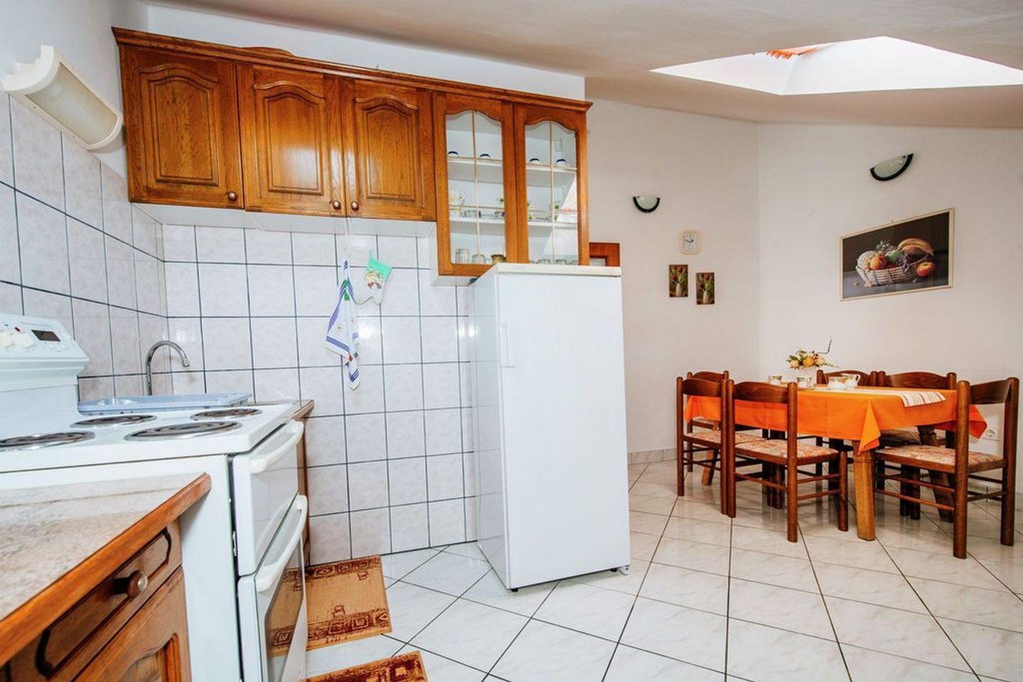 A compact kitchen with wooden cabinets, a white refrigerator, a stove, and a dining area with a table and chairs.