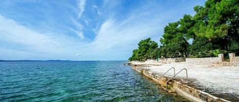 A clear blue sea with a rocky pier and trees.