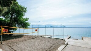 Una cancha de voleibol de playa con una red, el logotipo de Red Bull, y vistas al mar y montañas al fondo.