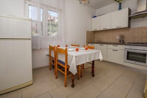 A kitchen with a table, chairs, a refrigerator, cabinets, and a window.