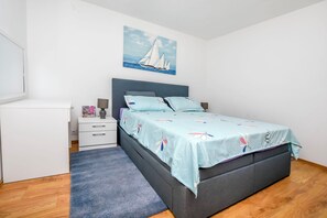 A bedroom with a bed, a nightstand, a dresser, and a painting of sailboats on the wall.