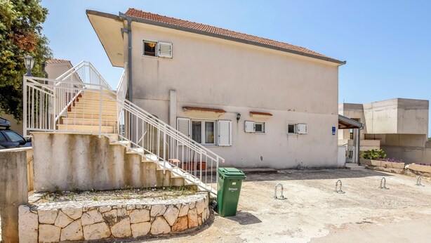 A two-story building with a stone staircase leading to the entrance, a green trash bin, and a concrete area with three metal faucets. - Apartments Apartmani Bebe (Razanj)