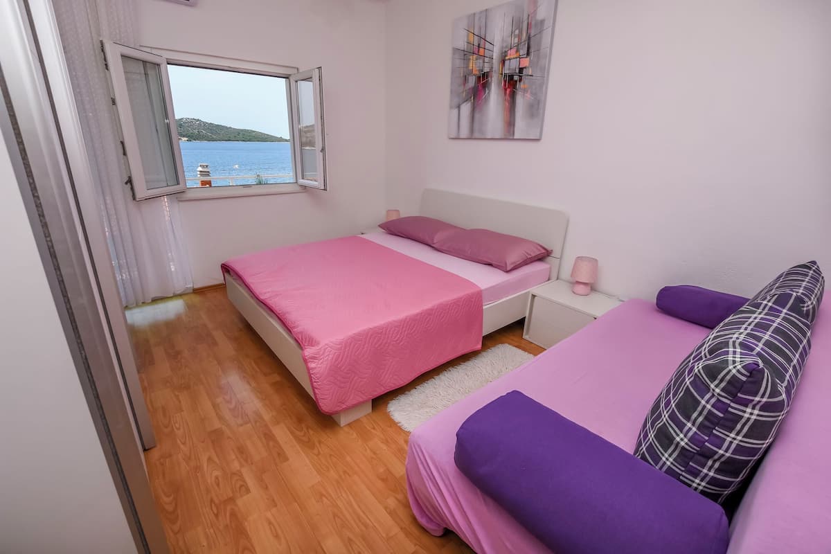 Un dormitorio con cama, una mesita de noche, una ventana con vista al mar y un cuadro en la pared.