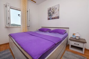 A bedroom with a bed, a nightstand, a window, and a painting on the wall.