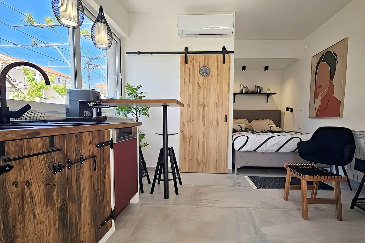 Une petite pièce comprenant un coin cuisine, un lit, une chaise et un tableau accroché au mur.
