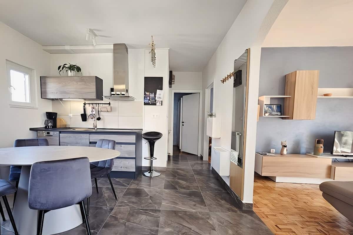Une cuisine moderne avec un coin repas, comprenant un îlot central, un revêtement de sol en carrelage foncé et des meubles contemporains.